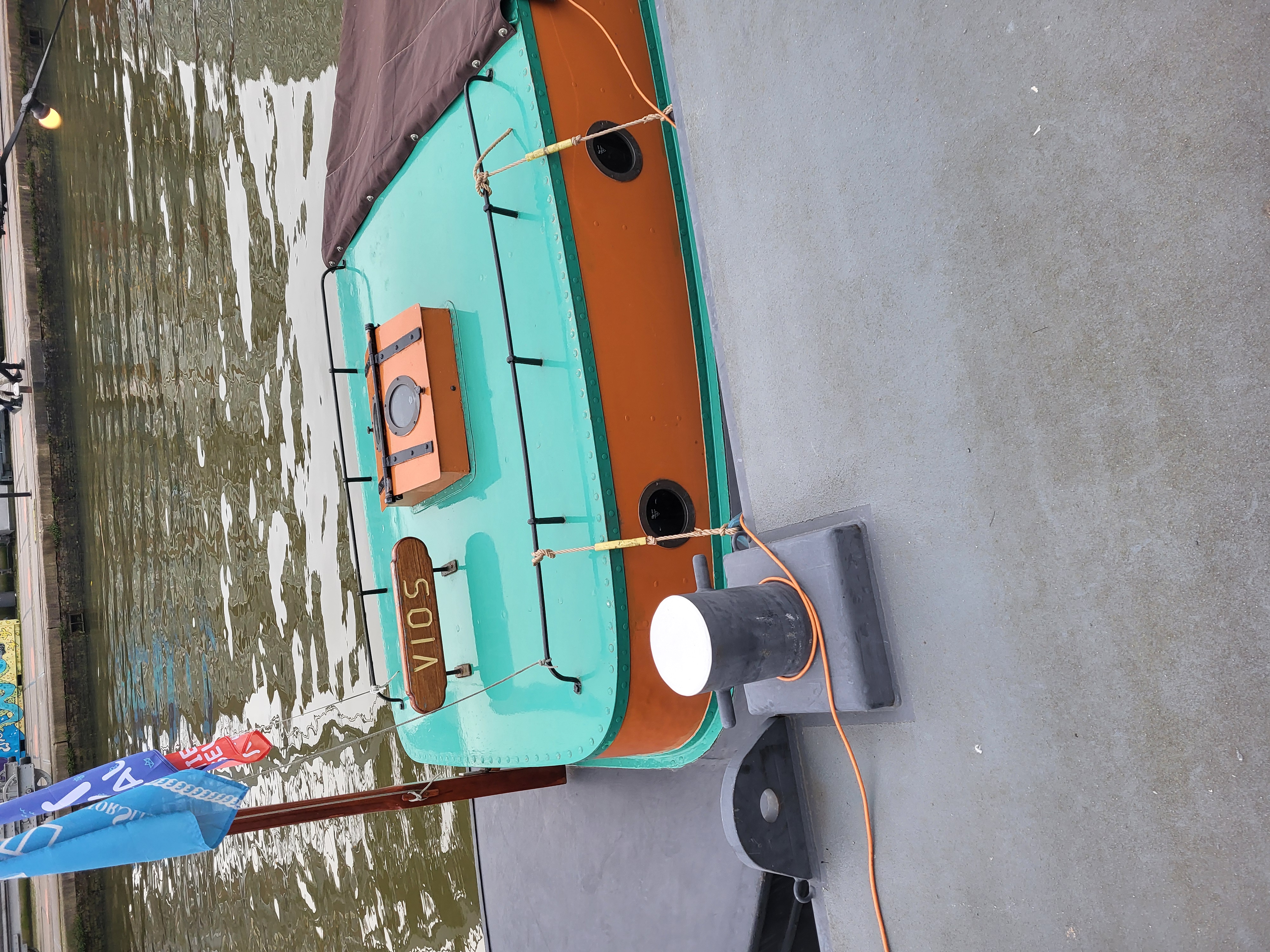 a photograph of a small orange and teal boat in a river.