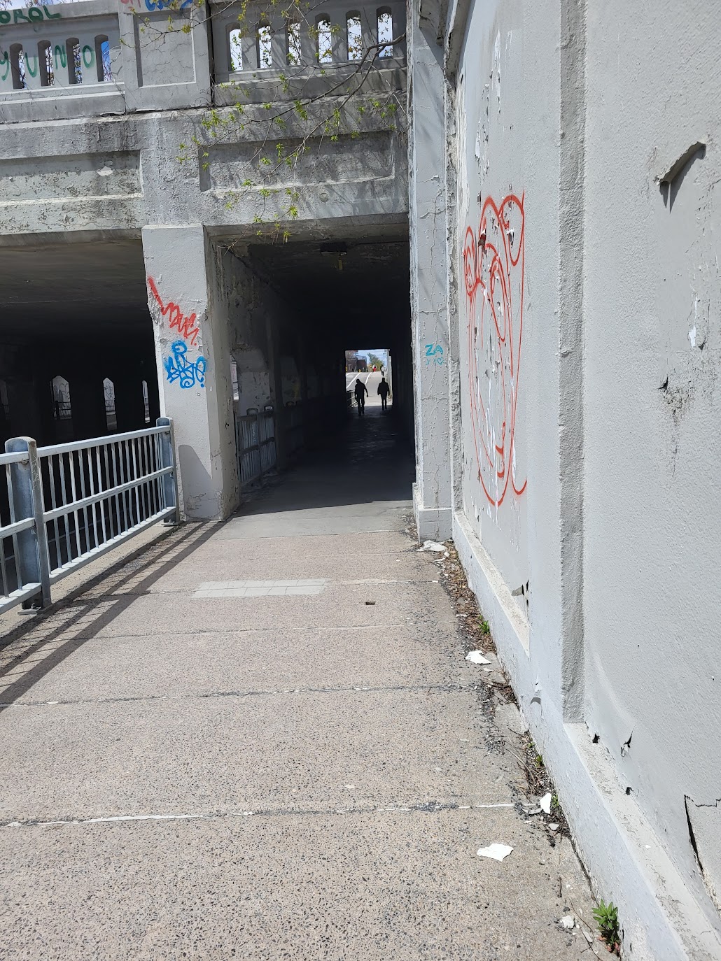 a tunnel going under a highway. Two shadowy figures stand inside.